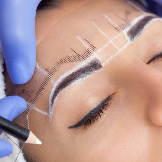 Permanent make-up for eyebrows of beautiful woman with thick brows in beauty salon. Closeup beautician doing  tattooing eyebrow.